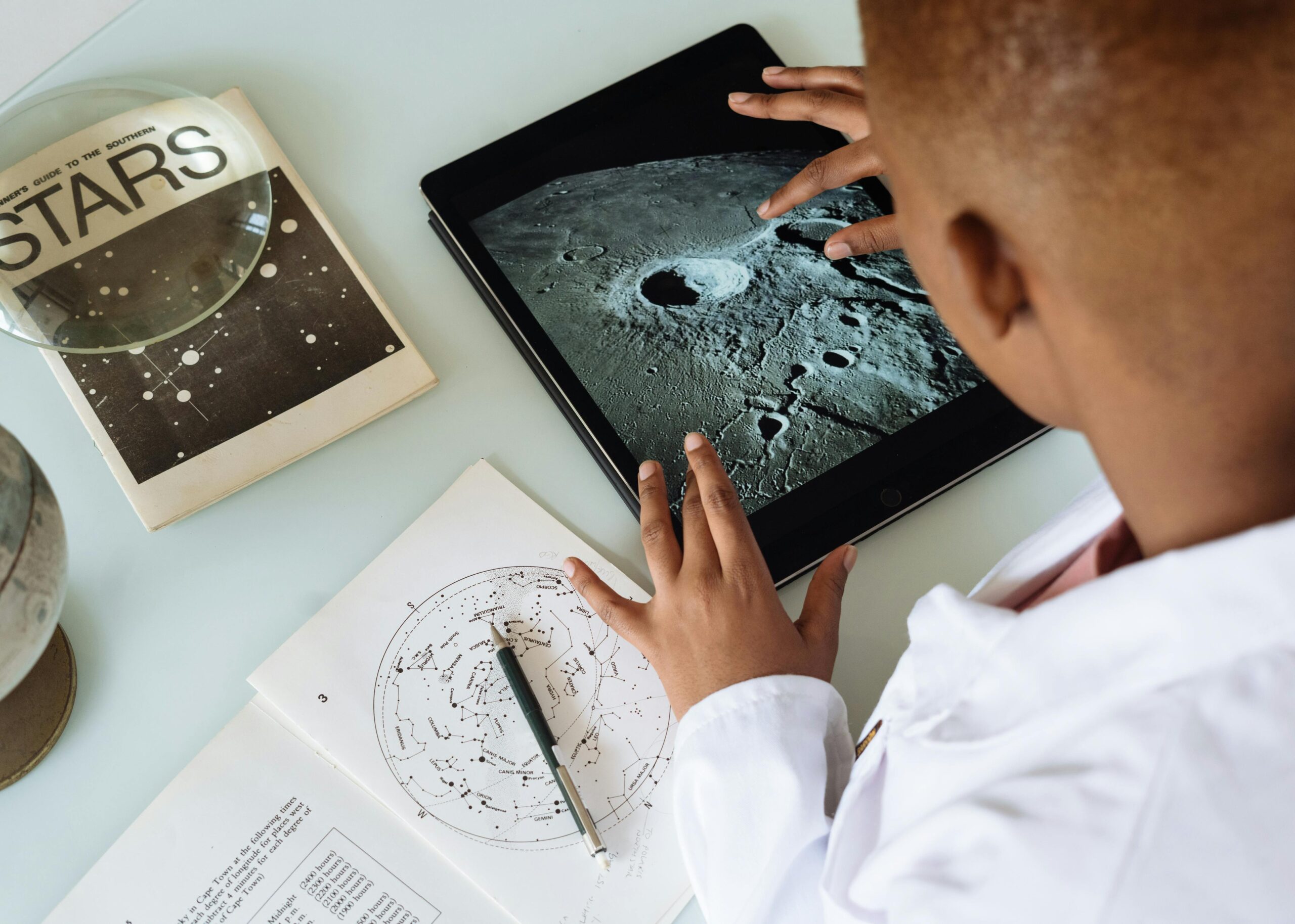 Child exploring moon craters on tablet surrounded by astronomy books and charts.